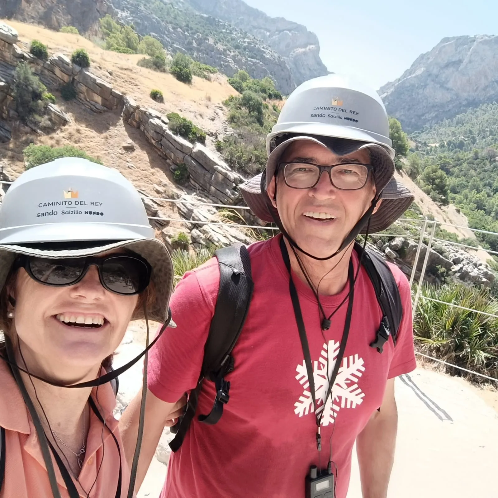 Tino y Cristina en el Caminito del Rey, con casco y sombrero, sonriendo ante el desfiladero